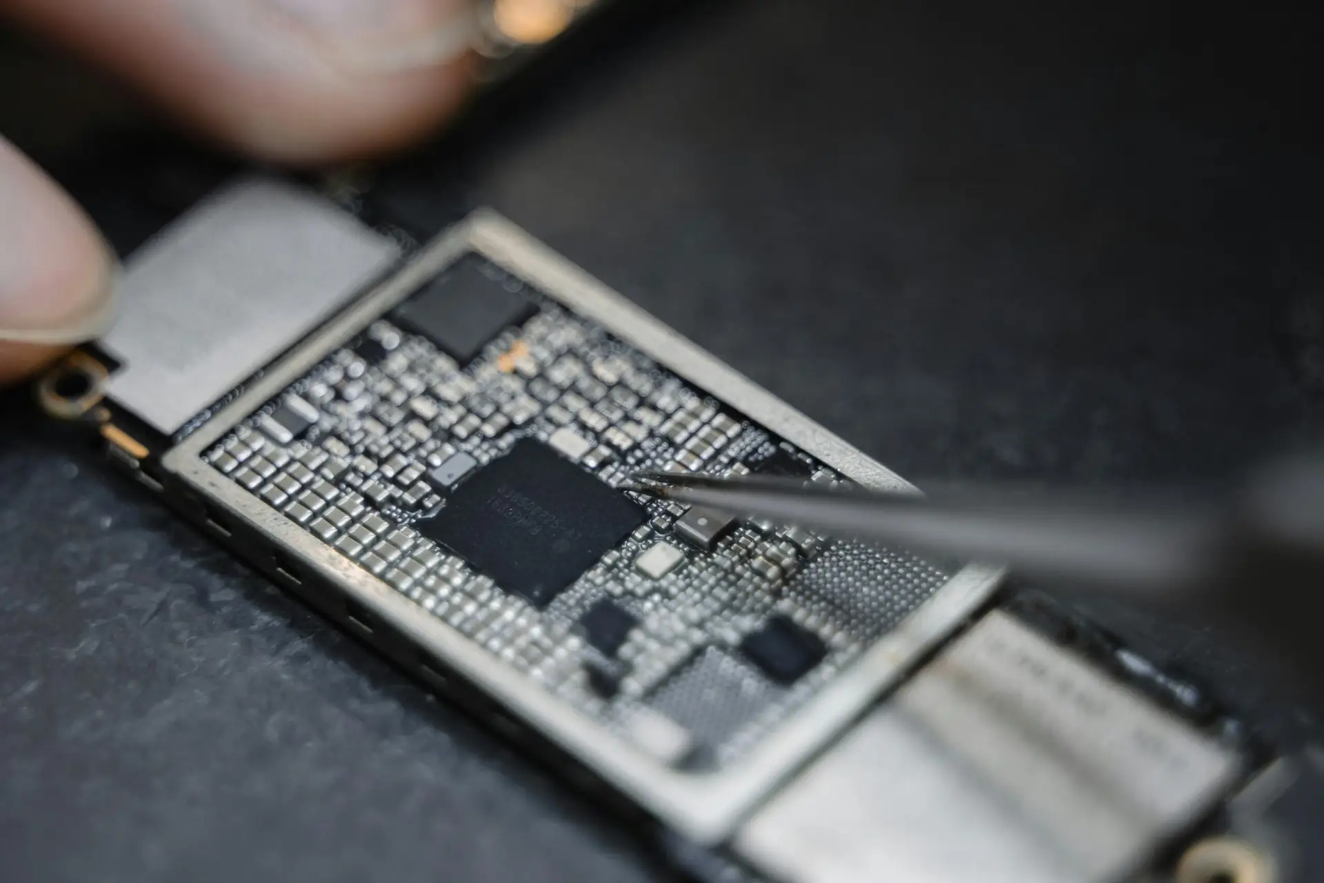 Detailed view of a technician using tweezers to fix an electronic circuit board.